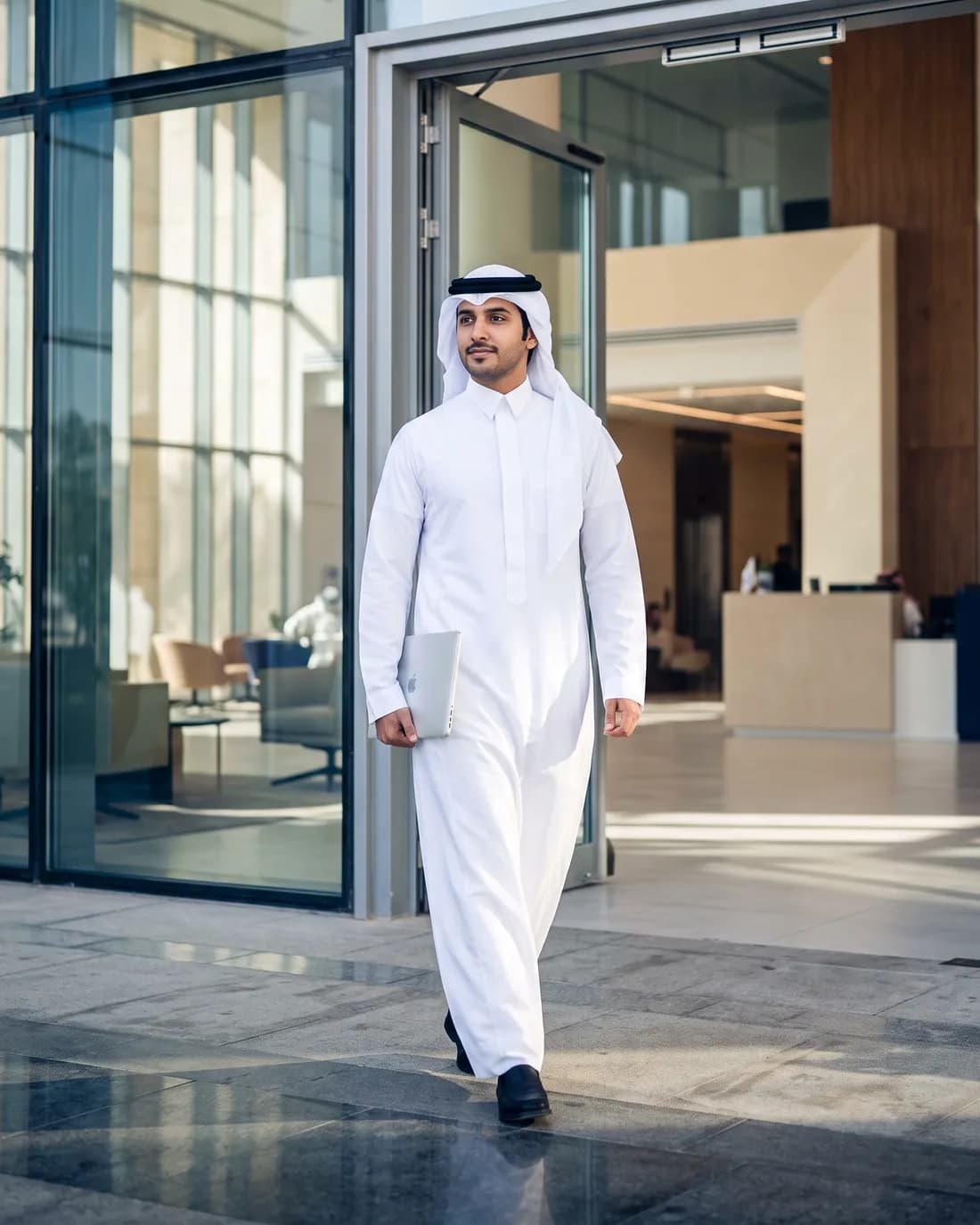 شاب سعودي بالثوب يخرج من مقر عمل حديث حاملاً حاسوبه